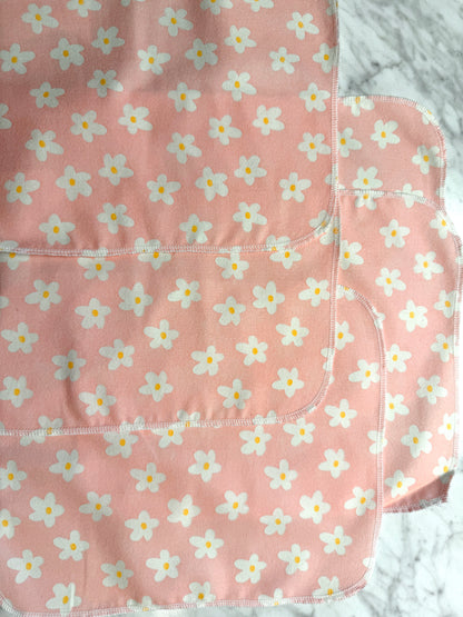 Four pink Not Paper Towels Bundles by Sustainable For Good, featuring white and yellow flower patterns, overlap on a gray marbled surface—these reusable towels are an eco-friendly alternative to single-use paper towels.