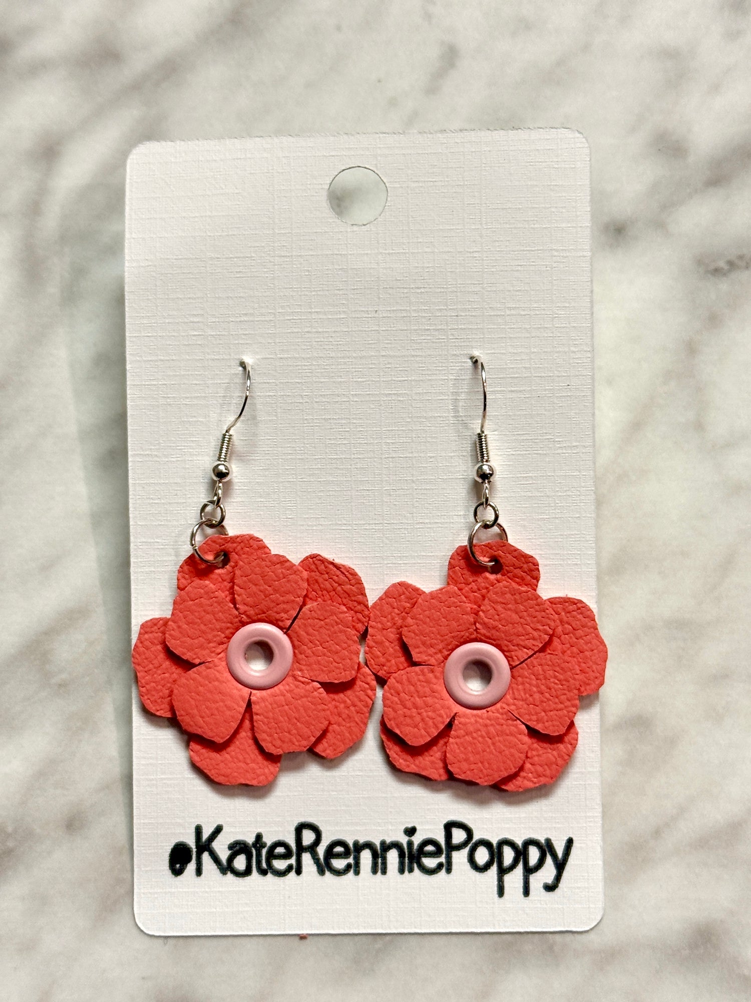 Red flower-shaped earrings on a white card with &