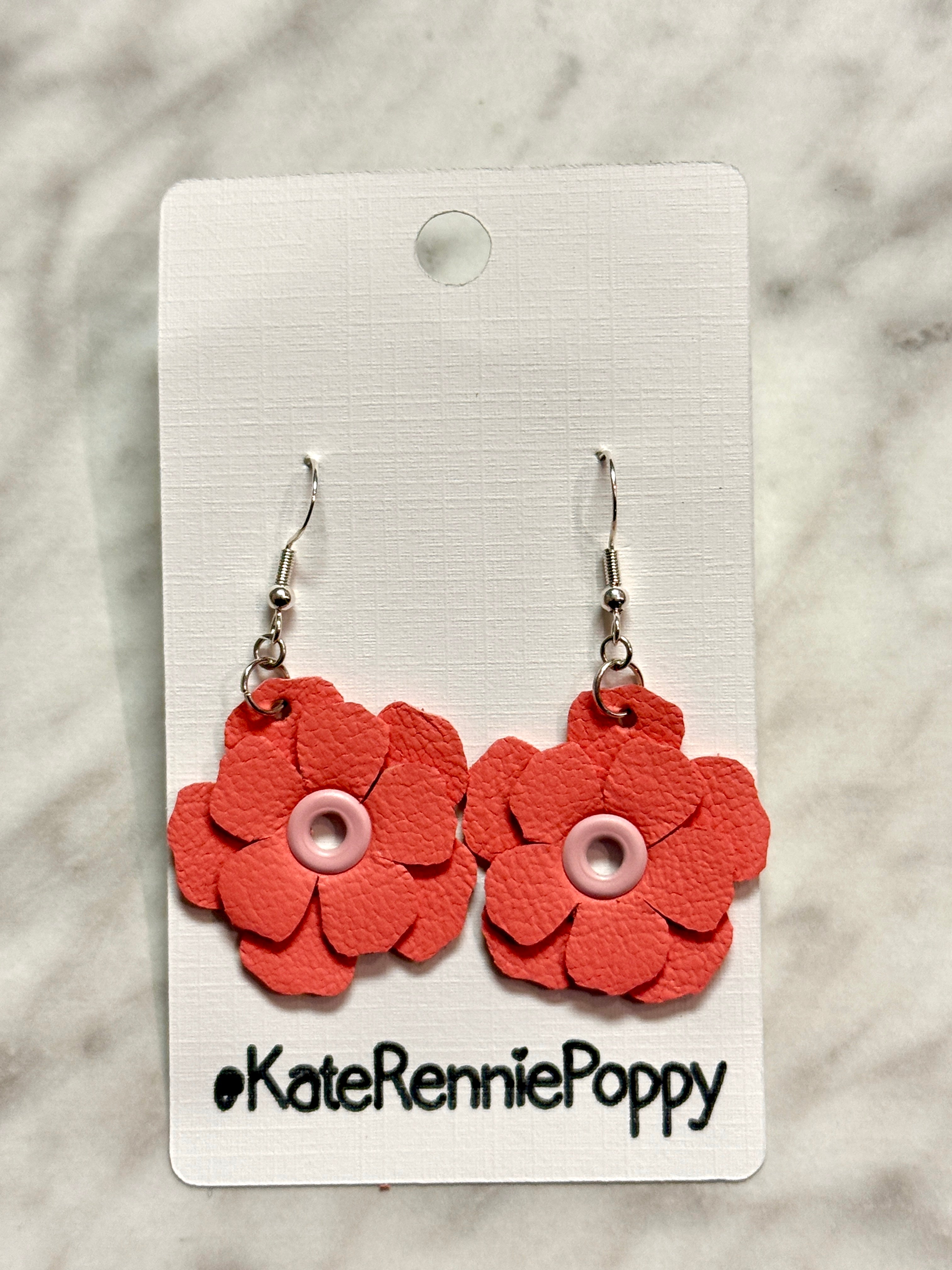 Red flower-shaped earrings on a white card with &