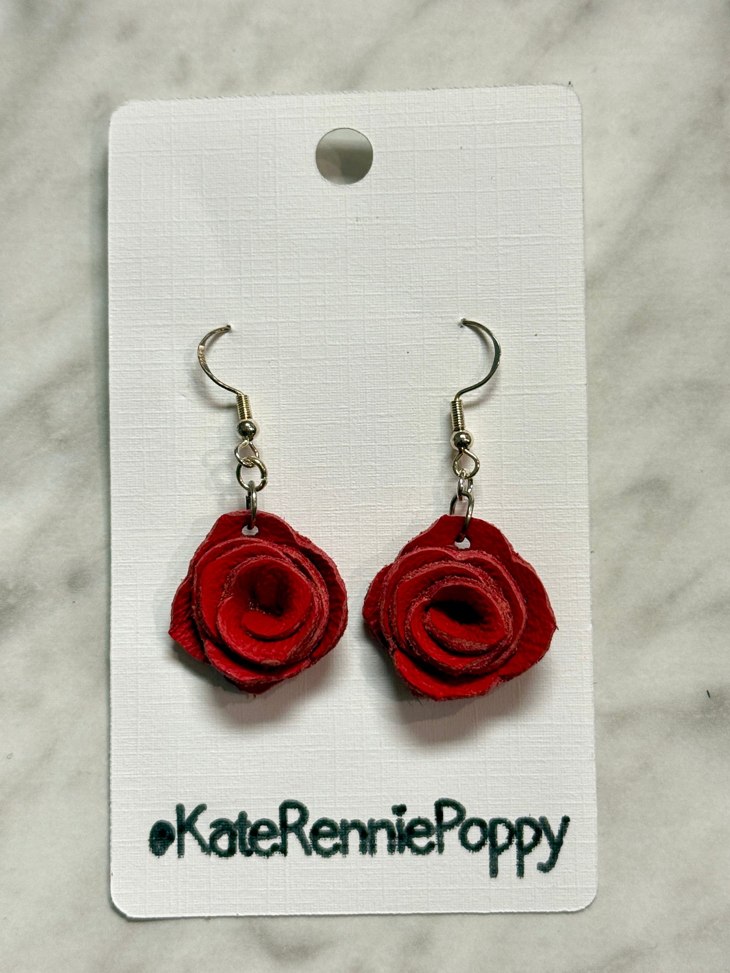 Red rose-shaped earrings on a white card with &