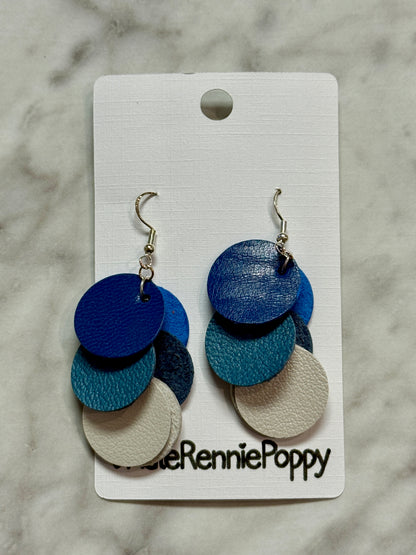 Blue and beige layered disc earrings on a Rennie Poppy branded card against a marble background