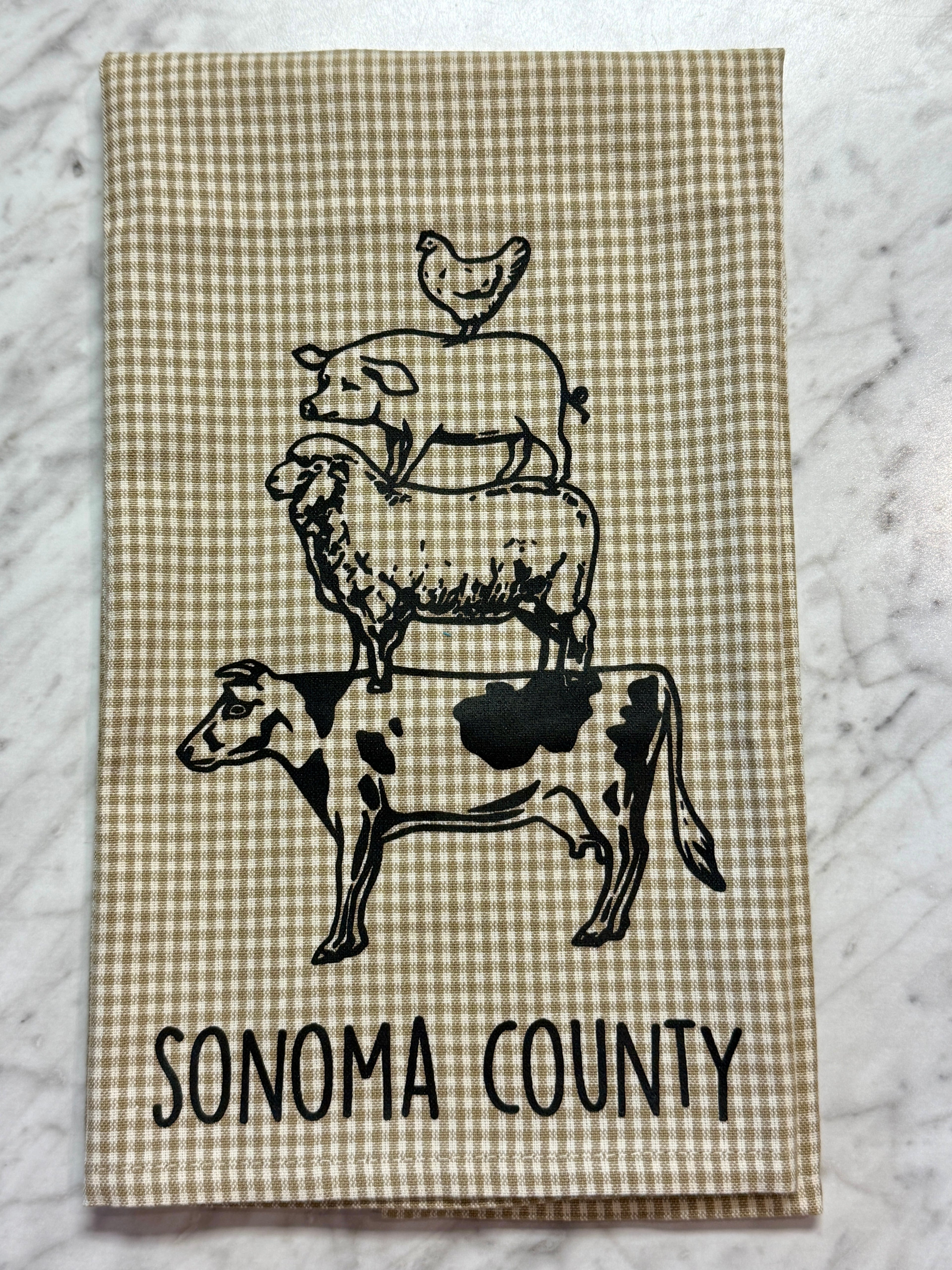 Tea towel with black and white illustrations of a cow, sheep, and chicken, and &