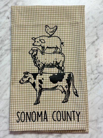 Tea towel with black and white illustrations of a cow, sheep, and chicken, and &