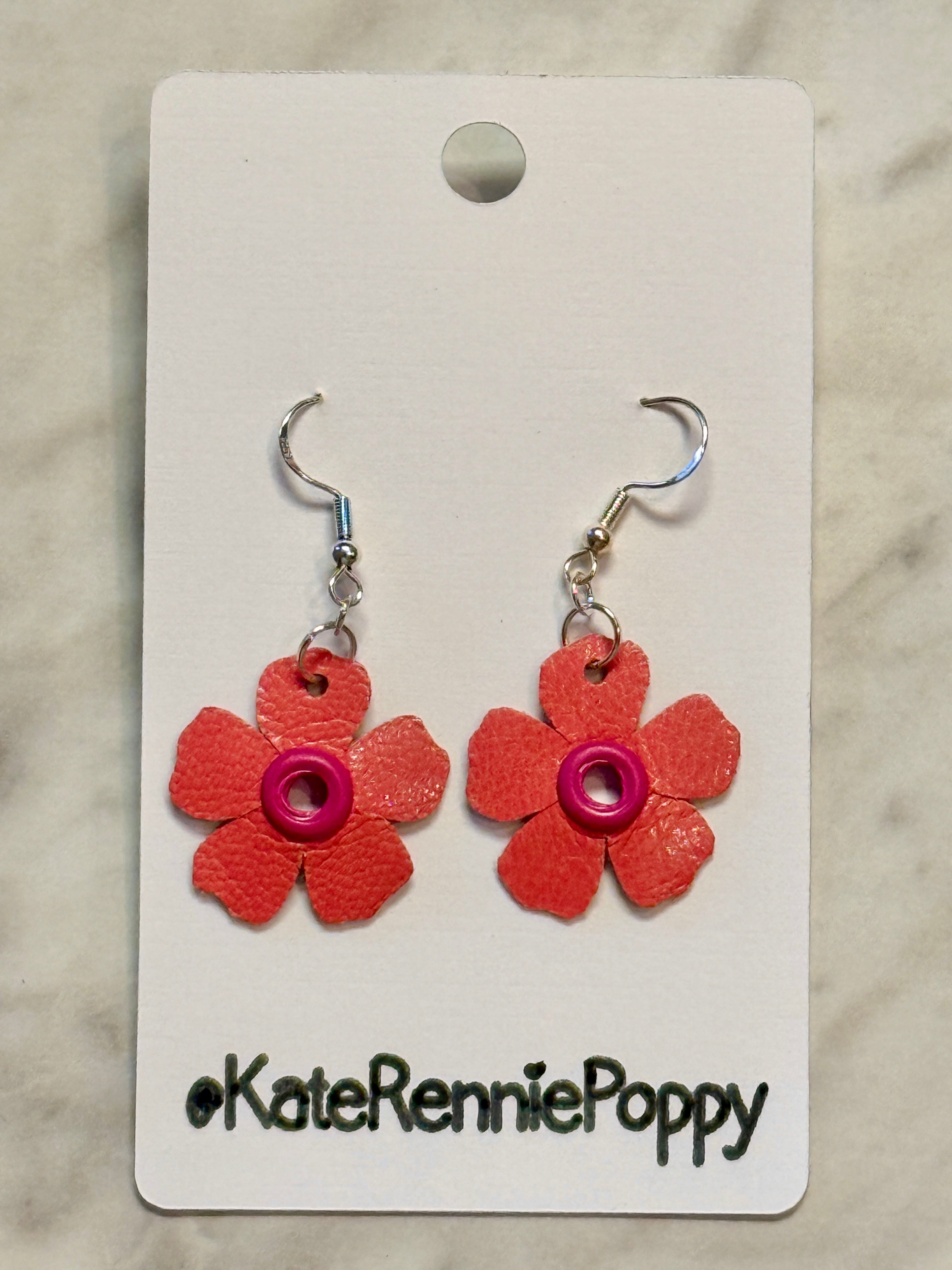 Red flower-shaped earrings with a pink center on a &