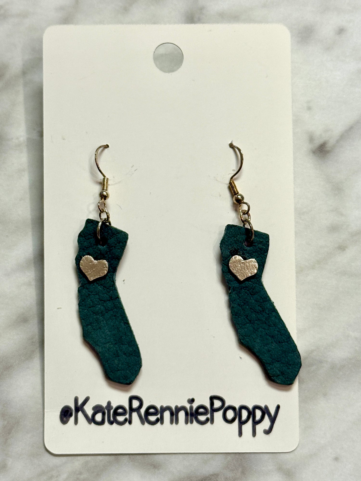 Sock-shaped earrings with heart details on a Kate Rennie Poppy card against a marble background.