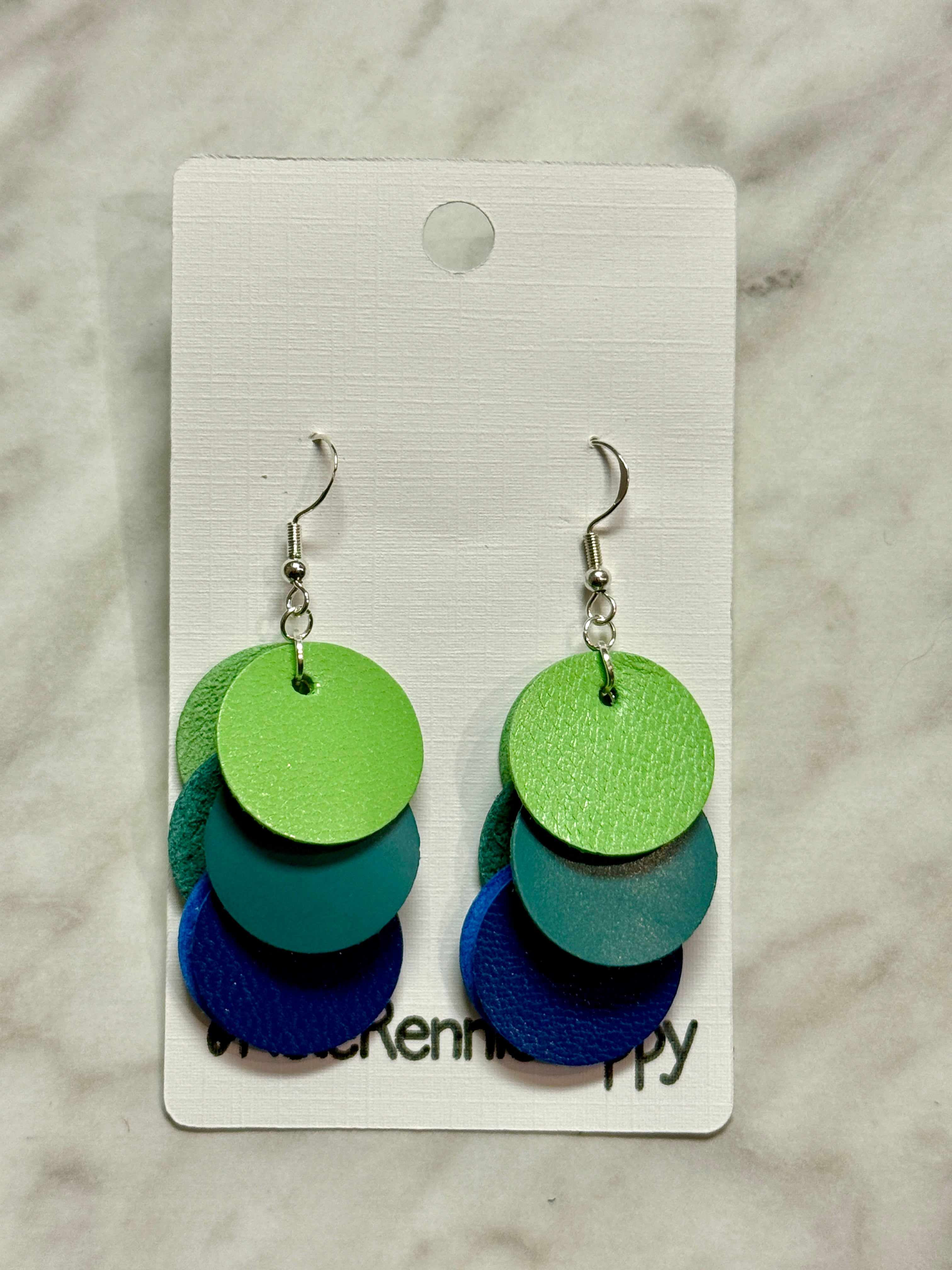 Colorful layered disc earrings on a branded card against a marble background