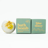 Bath bomb with yellow flowers next to its packaging on a white background