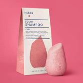Pink solid shampoo bar with packaging on a pink background