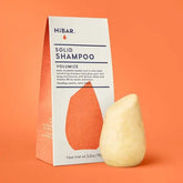 Solid shampoo bar and packaging on an orange background