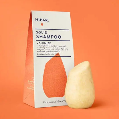 Solid shampoo bar and packaging on an orange background