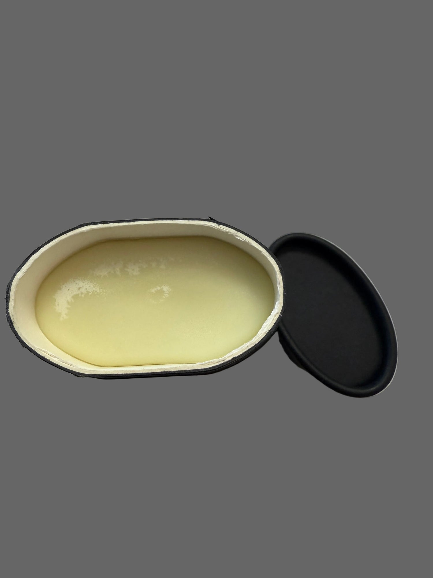 Bar of lotion in an open black container on a marble surface