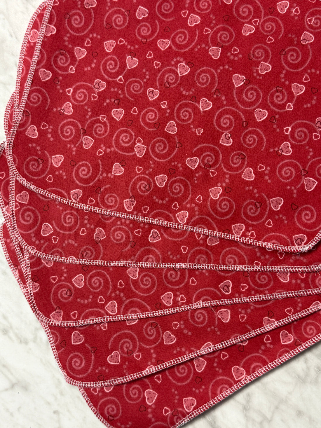 Red fabric with white heart patterns on a textured surface