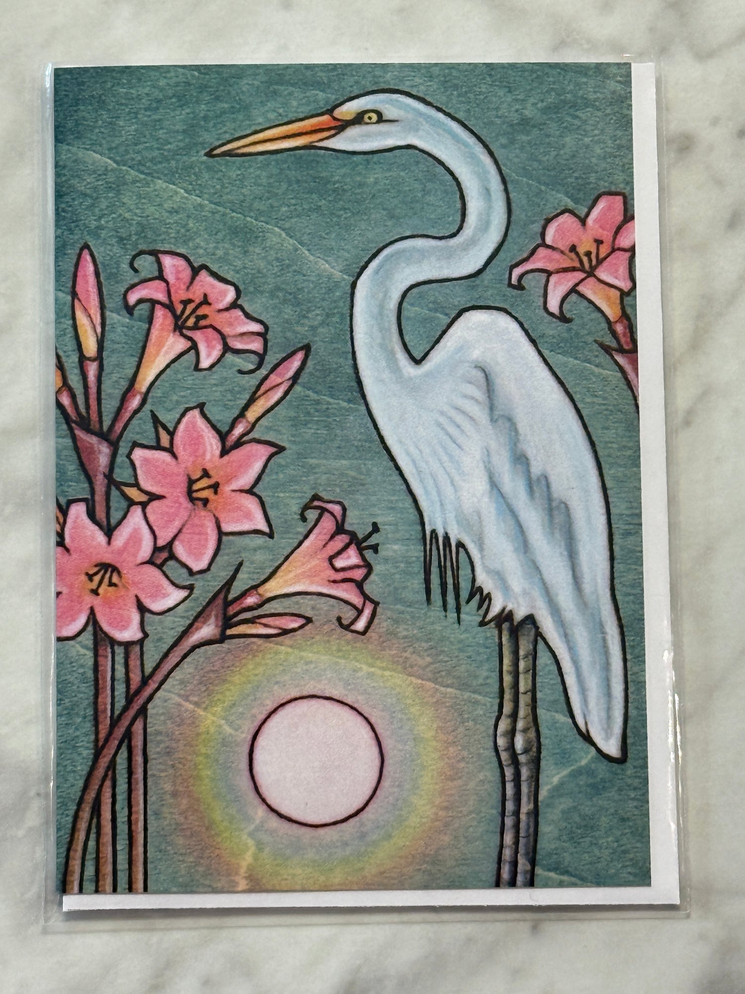 Card with a stylized illustration of an egret and pink flowers against a sunset background.