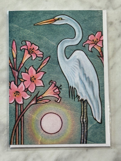 Card with a stylized illustration of an egret and pink flowers against a sunset background.