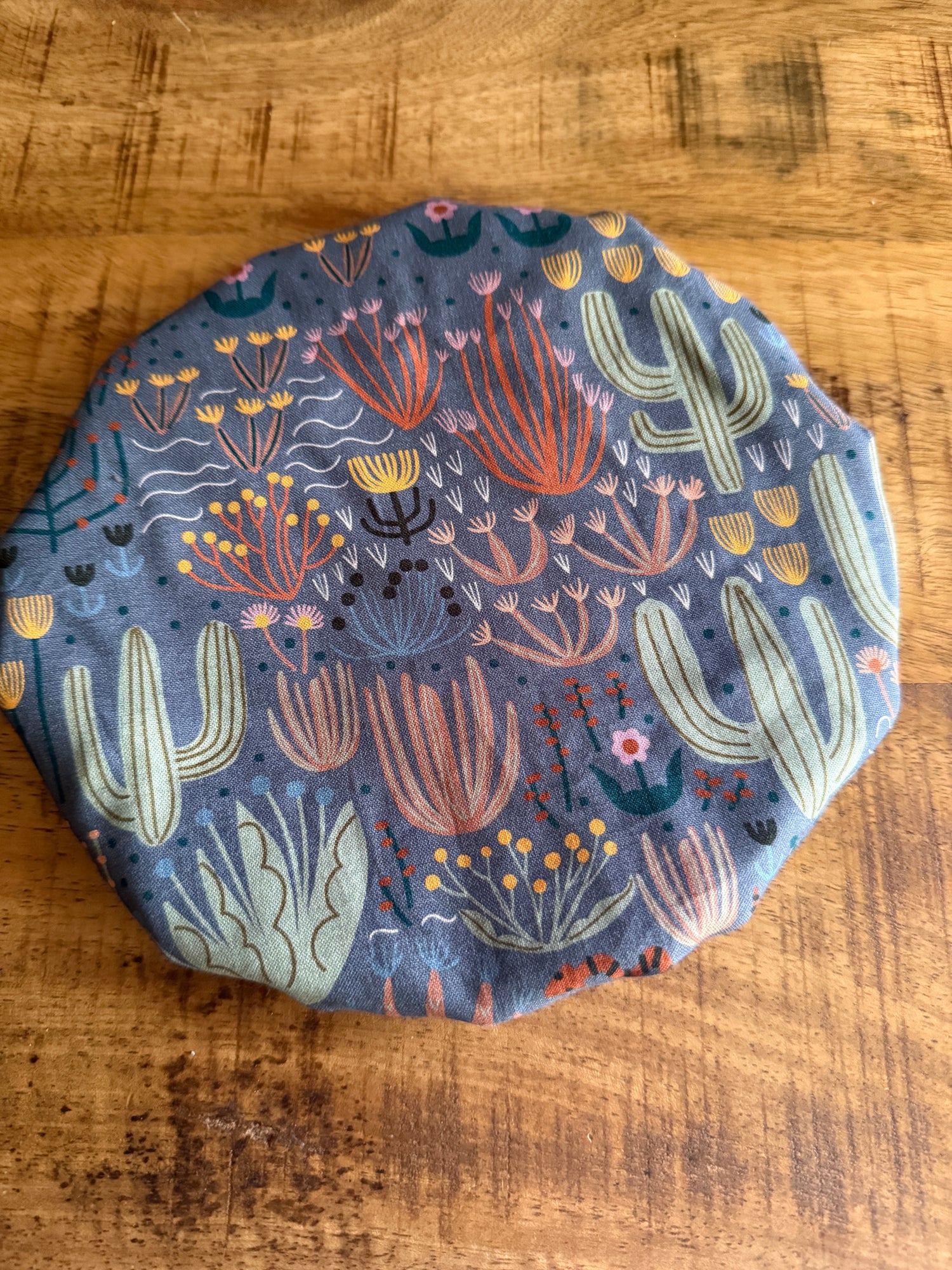 The Sustainable For Good Reusable Reversible Bowl Cover, featuring a colorful cactus and succulent pattern on gray, sits on a wooden surface—an eco-friendly touch for your plastic-free kitchen.