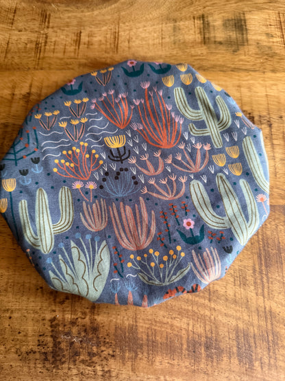 The Sustainable For Good Reusable Reversible Bowl Cover, featuring a colorful cactus and succulent pattern on gray, sits on a wooden surface—an eco-friendly touch for your plastic-free kitchen.