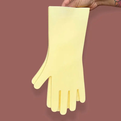 A hand holds up a pair of Keeps Silicone Cleaning Gloves against a plain mauve background.