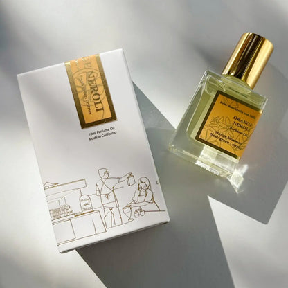 A perfume box with a gold label and simple line art sits beside a glass bottle labeled Roll On Perfume with a gold cap, both on a white surface with shadows—a sophisticated presentation that perfectly complements the Kyler Handcrafts Roll On Perfume and its phthalate-free fragrance.