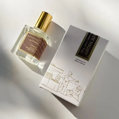 A Kyler Handcrafts Roll On Perfume with a gold cap rests beside its white box, adorned with minimalist line art of two people at a market stall. Sunlight highlights the elegant, handcrafted design.