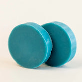 Two teal-colored shave soap bars on a light beige background