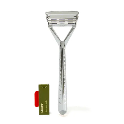 The Leaf Razor by Leaf features three stacked blades and stands upright next to a small green and red LEAF box with replacement blades, offering a plastic-free shaving option against a white background.