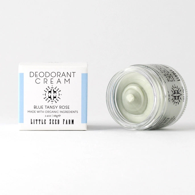 A jar of Little Seed Farm Deodorant Cream is open beside its white and blue box with black text. The aluminum-free cream inside is light green. Brand: Little Seed Farm.