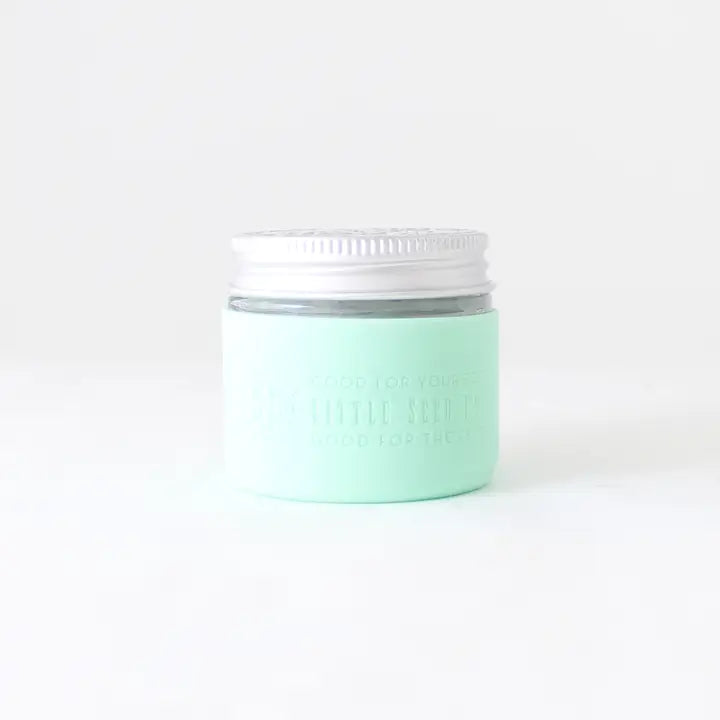 A mint green Protective Silicone Sleeve by Little Seed Farm rests on a plain white background. The sleeve, a sustainable alternative, features subtle embossed text on its side and fits snugly around jars.