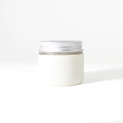 A small white cosmetic jar with a silver screw-on lid sits on a plain background. The mostly blank label highlights its eco-friendly design—perfect for use with the Little Seed Farm Protective Silicone Sleeve.