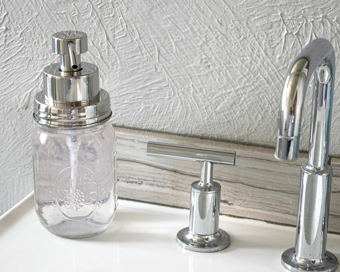 Clear glass soap dispenser with silver pump on a white surface