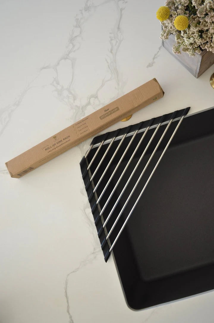 Black baking tray with metal cooling rack on a marble surface with a cardboard box and flowers in the background.