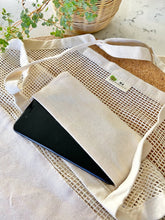 Black phone in a beige fabric pouch on a textured surface with a plant in the background
