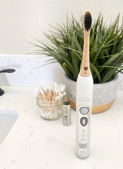 Electric toothbrush with bamboo handle on a bathroom counter next to a plant and other items.