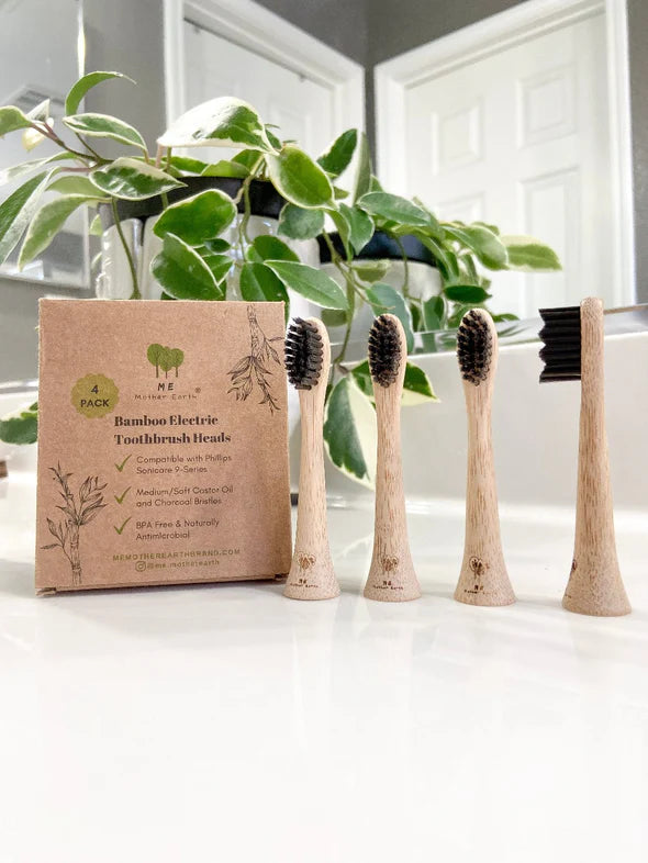 Bamboo electric toothbrush heads with packaging on a white surface with plants in the background