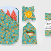 green beeswax wraps with pua flowers on it wrapping a tray of watermelon, a half lemon, and a sandwich