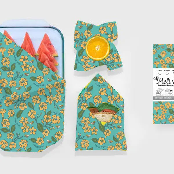 green beeswax wraps with pua flowers on it wrapping a tray of watermelon, a half lemon, and a sandwich