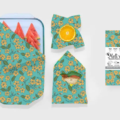 green beeswax wraps with pua flowers on it wrapping a tray of watermelon, a half lemon, and a sandwich