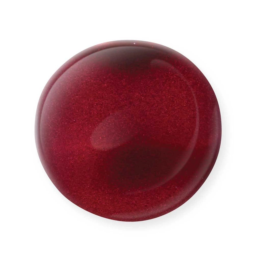 A close-up of a single drop of deep red, shimmery Mineral Fusion Nail Polish by Mineral Fusion against a white background captures the essence of clean beauty and non-toxic nail color.