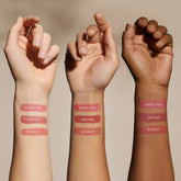 Three forearms of varying skin tones display swatches of three Minori Mini Cream Blush and Highlighter shades—Sweet Pea, Orchid, and Scarlet—vertically on each arm against a neutral background, highlighting sustainable beauty.