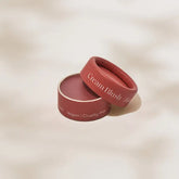 A round Minori Mini Cream Blush and Highlighter with a partially removed lid rests on a textured surface. The dusty rose packaging is labeled vegan, cruelty-free, reflecting Minori’s commitment to sustainable beauty.