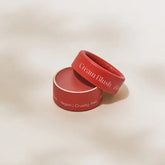 A round, red container of Minori Mini Cream Blush and Highlighter with its lid tilted aside. The packaging reads Cream Blush and Vegan | Cruelty-free, showcasing sustainable beauty on a soft, neutral background.