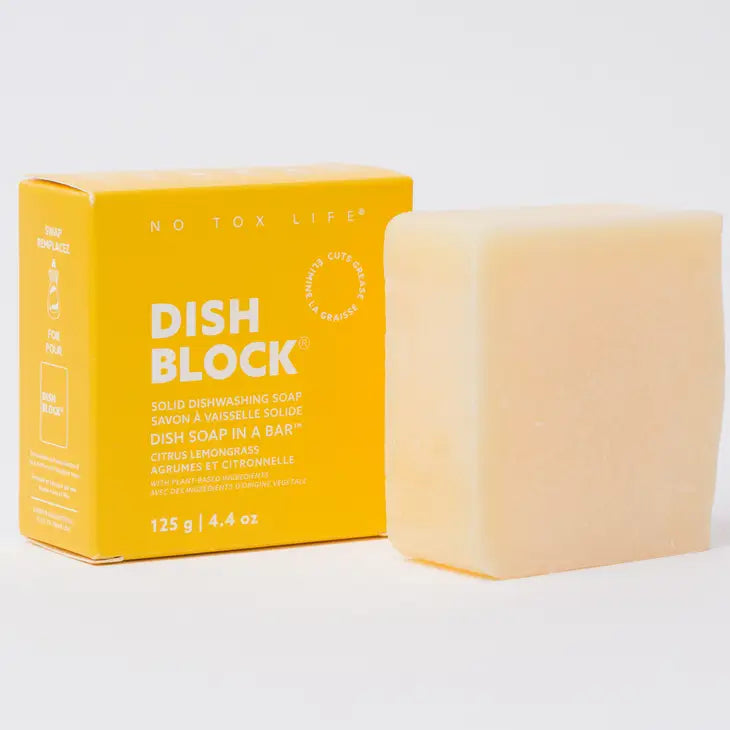 A rectangular yellow box labeled No Tox Life DISH BLOCK® 4.4 oz concentrated dishwashing soap stands by a pale bar; the vegan citrus lemongrass-scented soap weighs 125 g (4.4 oz).