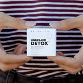 A person in a maroon and white striped shirt holds a No Tox Life Underarm Detox Bar, a 0.7 oz vegan, cruelty-free skincare product ideal for natural deodorant routines.