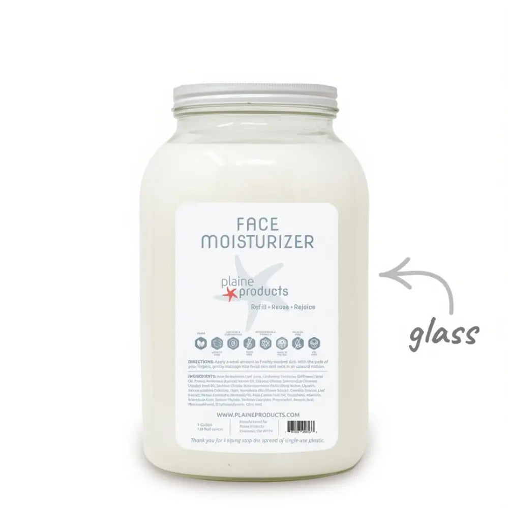 A large glass jar labeled “Bulk Face Moisturizer - Plaine” from Plaine Products, filled with white moisturizer. The label displays product details, and an arrow points to the glass jar to highlight its sustainable packaging. This renewing face moisturizer is vegan and cruelty-free, providing a gentle, eco-conscious option for your skincare routine.