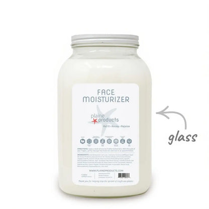 A large glass jar labeled “Bulk Face Moisturizer - Plaine” from Plaine Products, filled with white moisturizer. The label displays product details, and an arrow points to the glass jar to highlight its sustainable packaging. This renewing face moisturizer is vegan and cruelty-free, providing a gentle, eco-conscious option for your skincare routine.