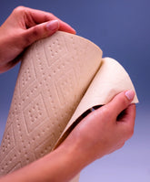 A person’s hands tear a sheet from a roll of Plant Paper Towels by Plant Paper, made from unbleached bamboo, against a plain blue background.