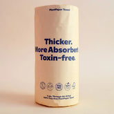 A roll of Plant Paper Towels by Plant Paper, unbleached with beige packaging and bold blue text: Thicker. More Absorbent. Toxin-free. Eco-friendly icons and certifications are displayed at the bottom of the pack.