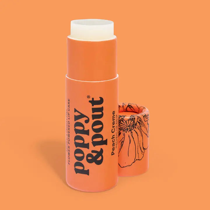 A Poppy &amp; Pout Lip Balm in the Peach Creme flavor, featuring an orange tube with black text and a floral design on the cap, displayed against an orange background.