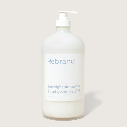 A clear pump bottle labeled Rebrand holds Bulk Face Sunscreen SPF 30, a refillable mineral sunscreen with zinc oxide and broad spectrum protection, shown against a plain light background.