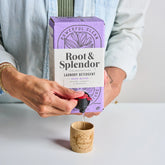 Person pouring Root & Splendor laundry detergent into a wooden container.