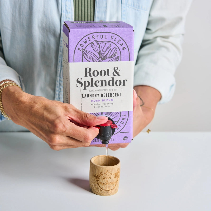 Person pouring Root &amp; Splendor laundry detergent into a wooden container.